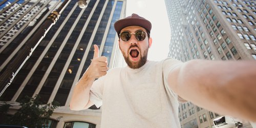 A man taking a selfie between buildings confidently opening his mouth widely